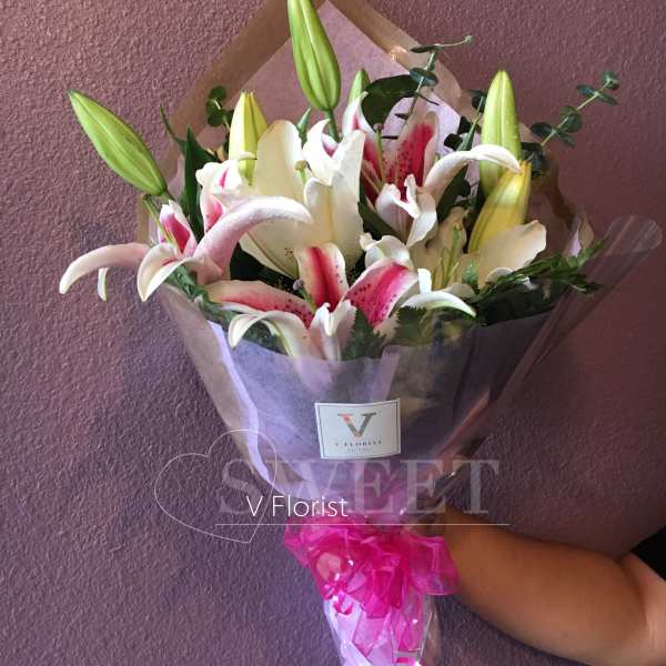 Hand-tied bouquet of pink and white lilies with buds, wrapped in clear paper with a bright pink ribbon bow