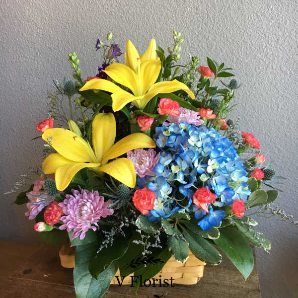 Basket arrangement with yellow lilies, blue hydrangeas, and pink flowers