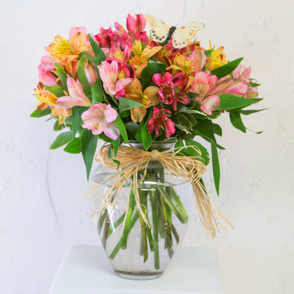 Bouquet of pink and yellow alstroemeria in a glass vase with a butterfly pick