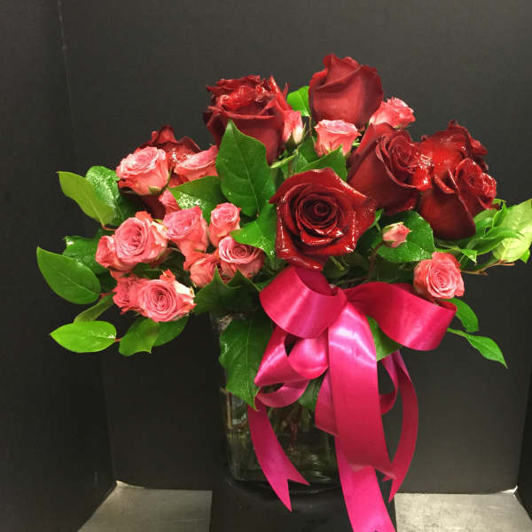 Red and pink roses arranged in a glass vase with a pink ribbon