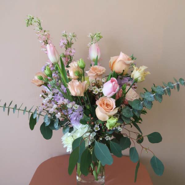 Mixed pastel bouquet in a clear glass vase with roses and tulips