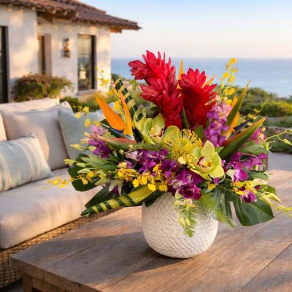 Tropical flower arrangement in a white textured vase on a wooden table