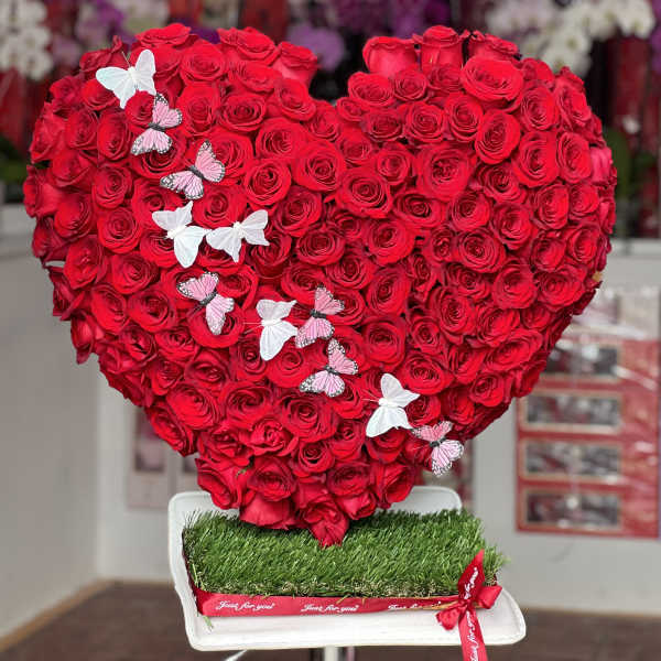 Heart-shaped arrangement of red roses with butterfly decorations on a white base