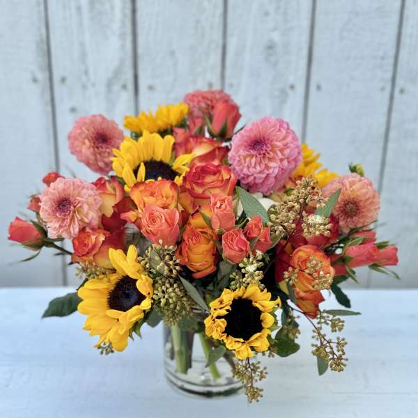 Bouquet of pink and orange roses with yellow sunflowers in a glass vase