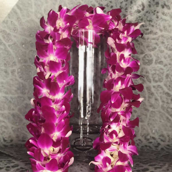 Purple orchid lei draped around a clear glass vase