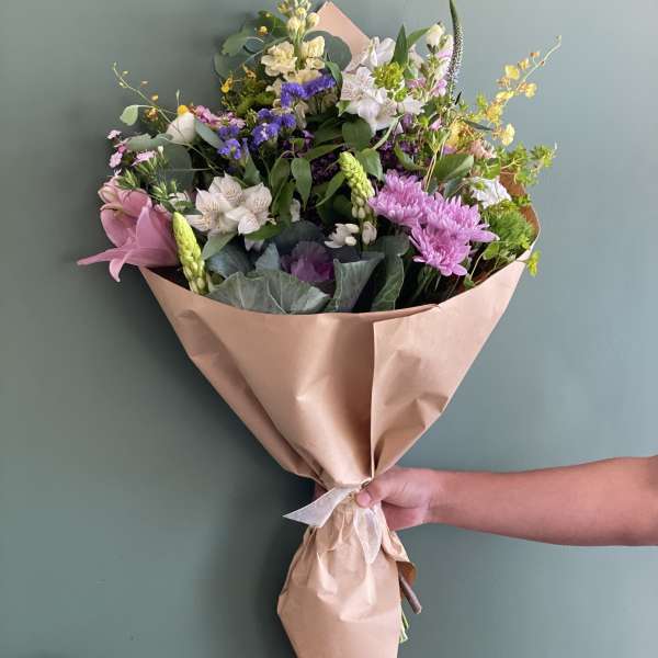 Hand-tied bouquet of mixed pink, white, purple, and yellow flowers in kraft paper