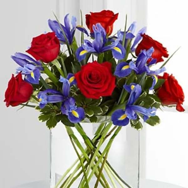 Red roses and blue irises in a clear glass vase