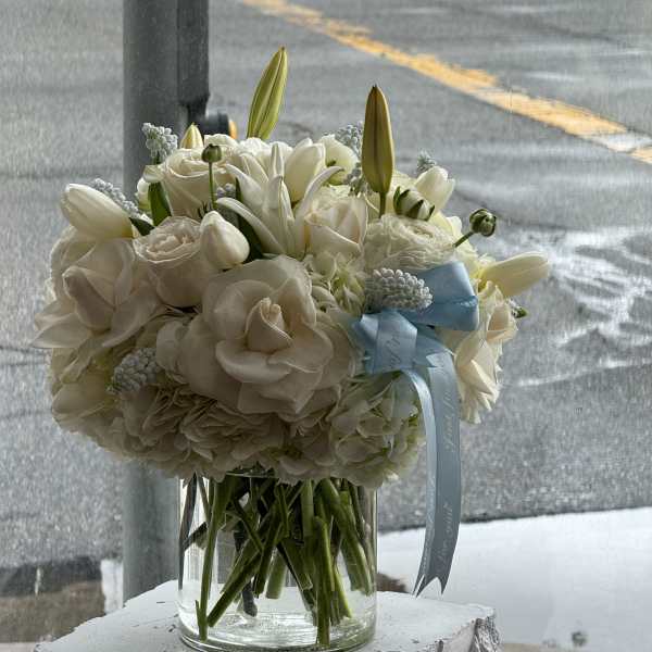 White bouquet in a clear glass vase with a blue ribbon