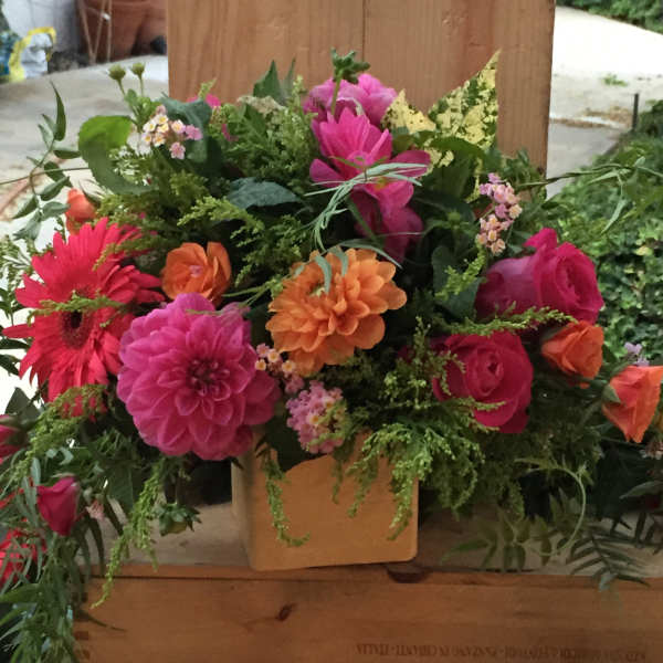 Bright mixed bouquet in a square vase with pink, orange, and red blooms