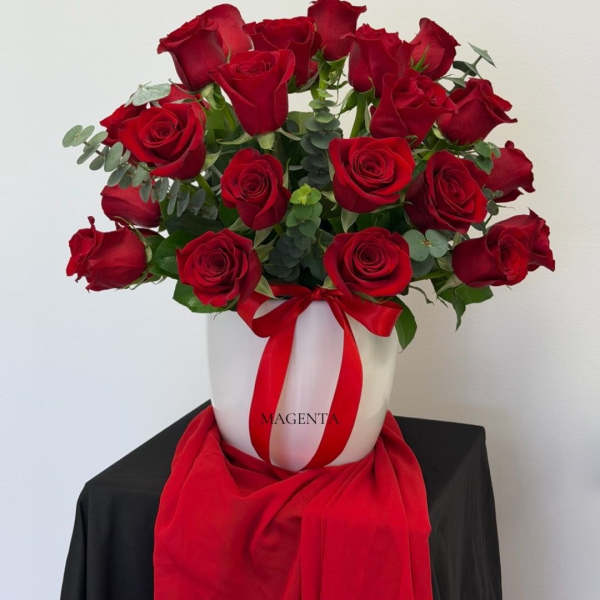 Red roses arranged in a white hatbox with a red ribbon
