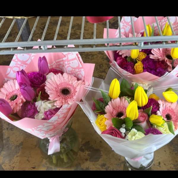 Three mixed bouquets with pink gerberas, tulips, and roses in pink and white wrap