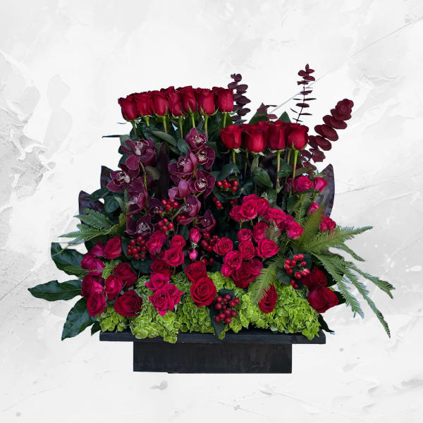Large arrangement of red roses, orchids, and greenery in a black container