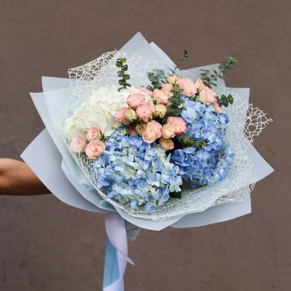 Hand-tied bouquet of blue hydrangeas, pink spray roses, and white blooms