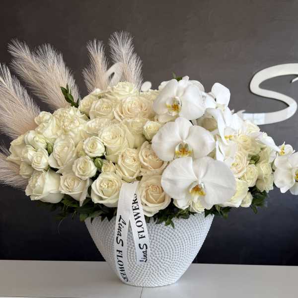 Cream roses and white orchids arranged in a textured white vase.