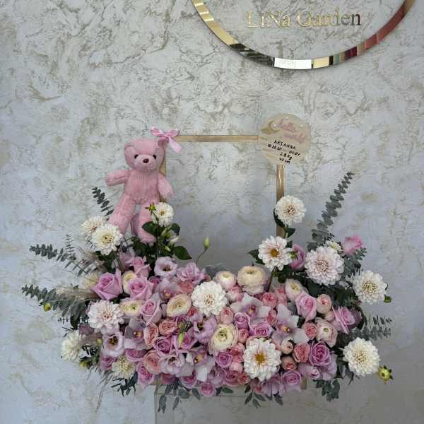 Pink and white rose arrangement in a low box with mums, lisianthus, eucalyptus, and a small pink teddy bear on a handle.