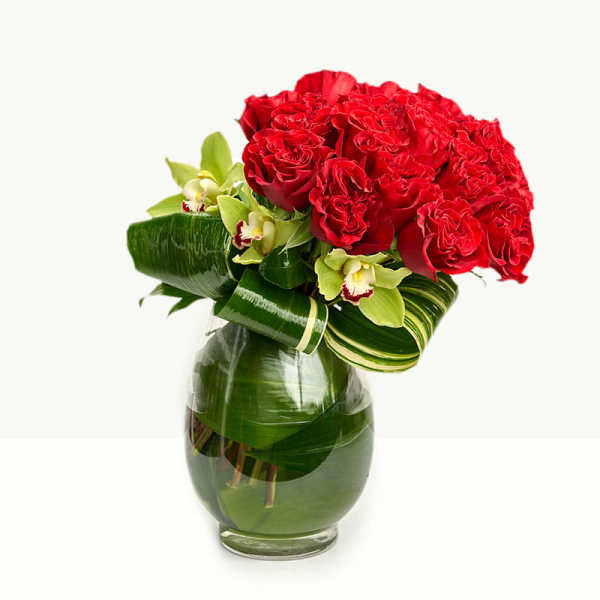Red roses and green orchids arranged in a glass vase