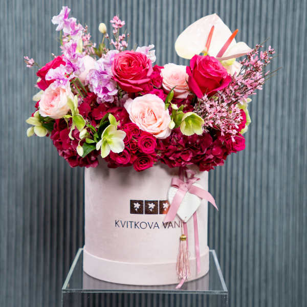 Pink and red floral arrangement in a round hat box with ribbon