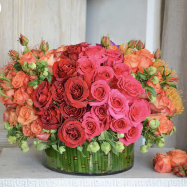 Round bouquet of pink, red, and peach roses in a glass vase