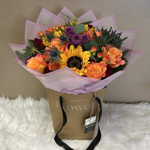 Bouquet of sunflowers, orange roses, and purple blooms in pink wrap