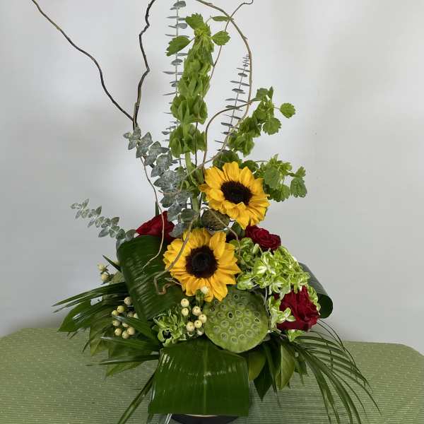 Tall floral arrangement with sunflowers and red roses in a black vase