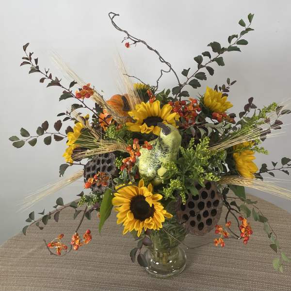 Sunflower arrangement in a glass vase with orange accents and decorative pods
