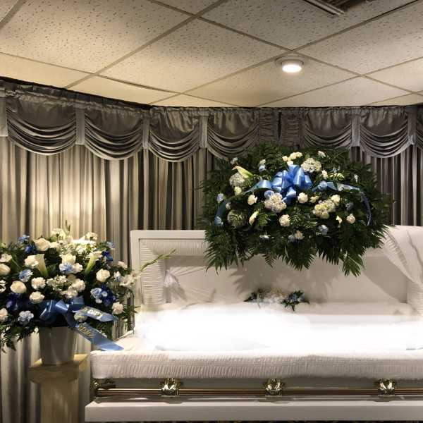 White casket with blue and white floral sprays in a funeral room
