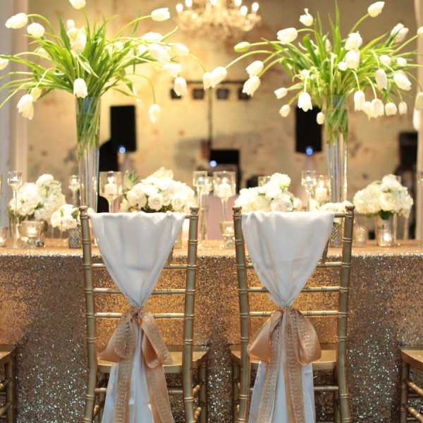 Tall white floral centerpieces on gold chairs at a decorated table