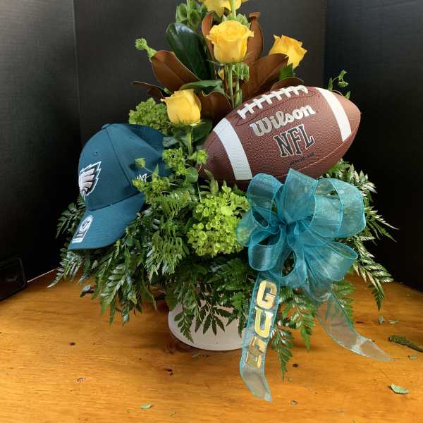 Yellow roses arranged with a football, cap, and teal ribbon in a white container