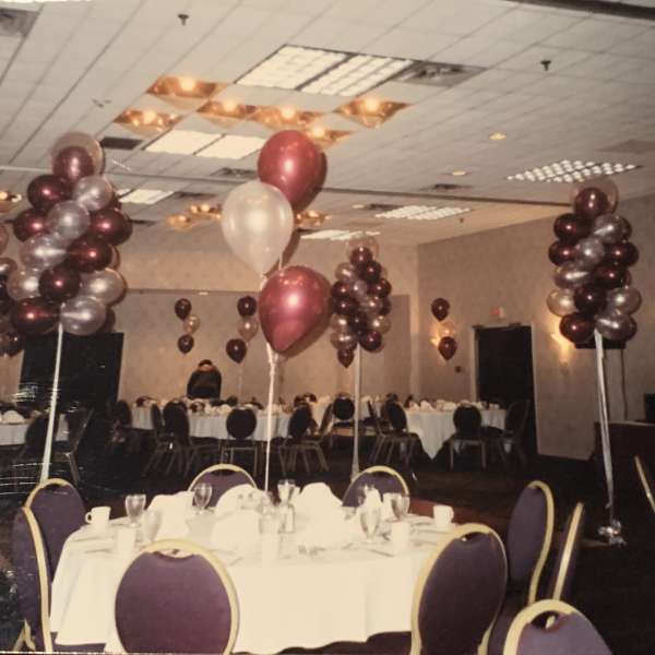 Balloon centerpieces in a banquet hall with round tables and purple chairs