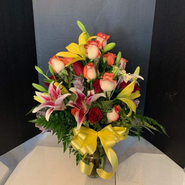 Mixed bouquet of roses and lilies in a glass vase with a yellow ribbon