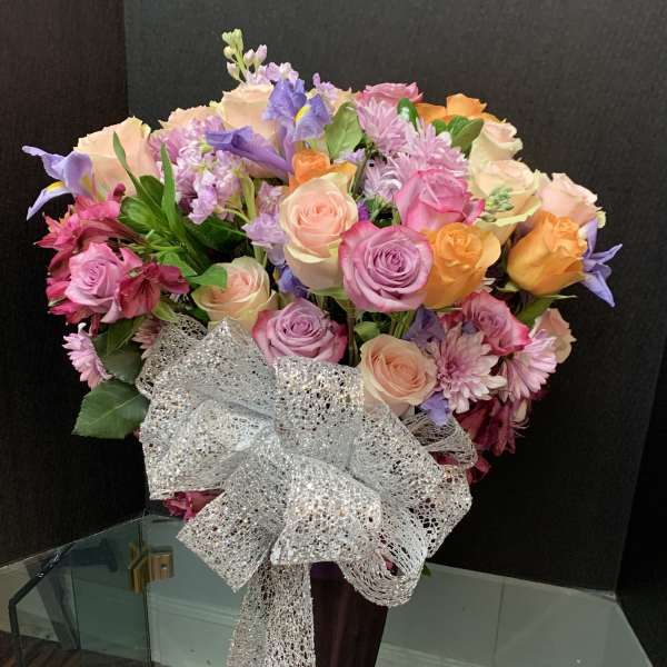 Mixed bouquet of pastel roses, irises, and chrysanthemums with a silver bow