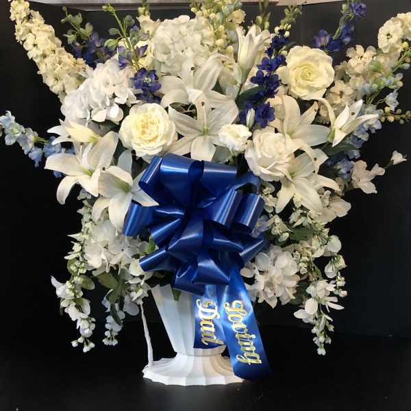 White and blue floral standing arrangement with a large ribbon on a pedestal vase