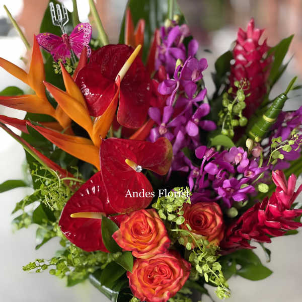 Tropical bouquet with red anthuriums, orange heliconia, and purple orchids in a black vase