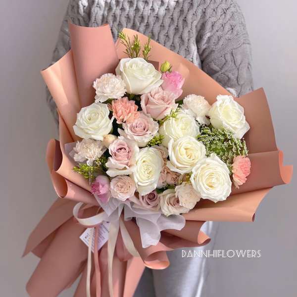 Bouquet of white and blush roses with carnations wrapped in peach paper