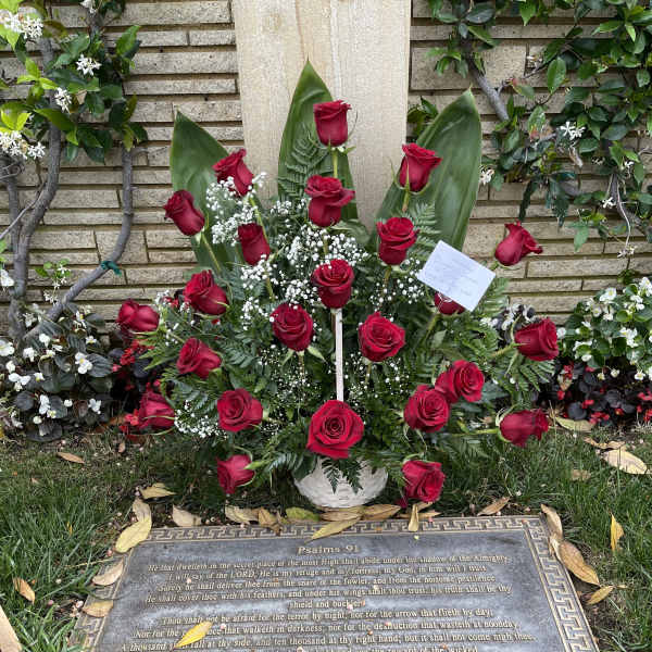 Red roses arranged in a white basket at a gravesite memorial