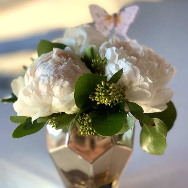 White peonies in a faceted glass vase with a butterfly pick