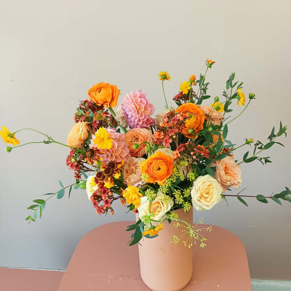 Mixed bouquet of orange, pink, and cream flowers in a blush vase