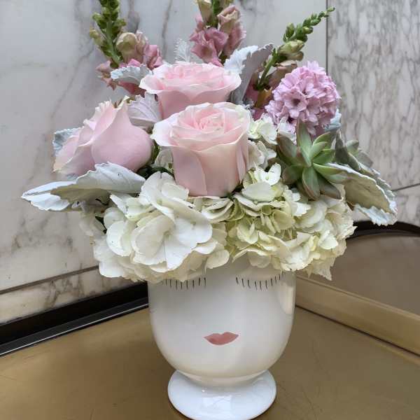 Pink roses and white hydrangeas arranged in a white vase with a face design.