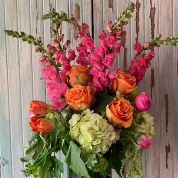 Orange roses and pink snapdragons in a tall glass vase