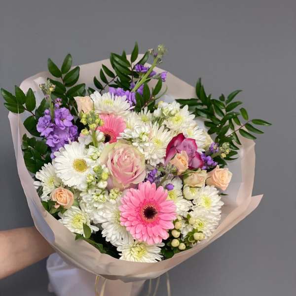 Hand-tied bouquet of pink, white, and purple flowers wrapped in pale paper