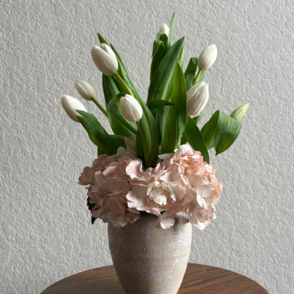 White tulips arranged with pale pink hydrangeas in a textured vase