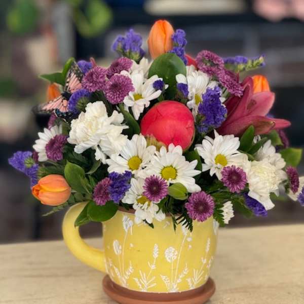 Mixed bouquet in a yellow mug with white daisies, purple blooms, and orange tulips