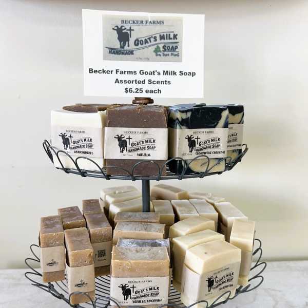 Two-tiered wire stand displaying assorted goat's milk soap bars with beige labels.