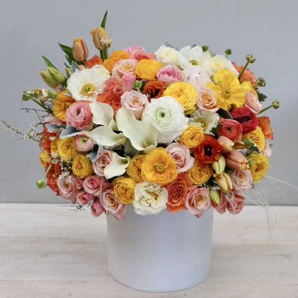 Mixed bouquet of pastel and bright flowers in a white cylindrical vase