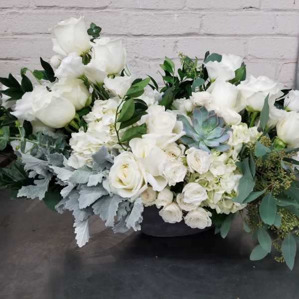 White rose arrangement with succulents and greenery in a low container