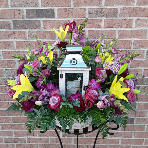 Floral funeral arrangement around a silver lantern in a basket