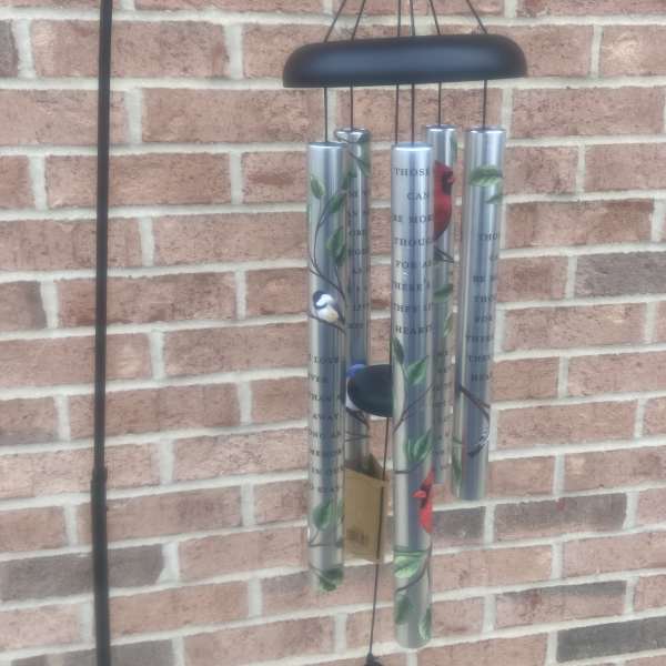 Black metal wind chime with silver tubes hanging against a brick wall