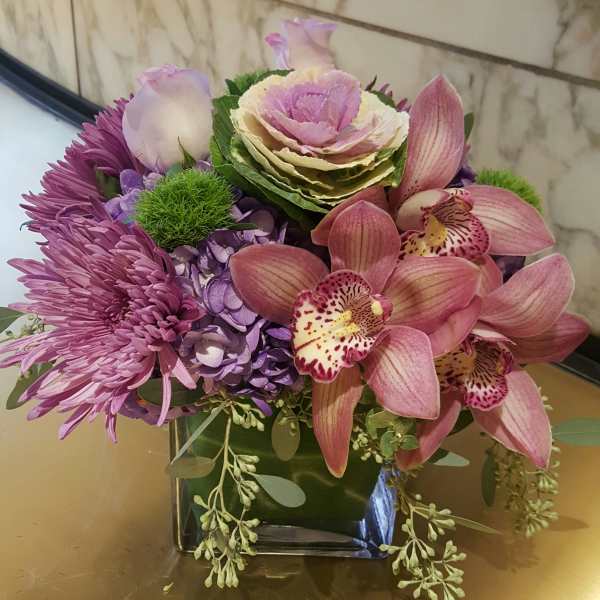 Purple and pink floral arrangement in a square glass vase