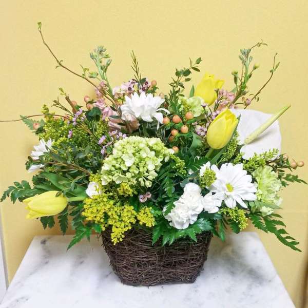 Mixed floral arrangement in a woven basket with yellow tulips and white daisies
