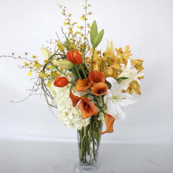 Tall bouquet of orange calla lilies, white lilies, and yellow orchids in a glass vase